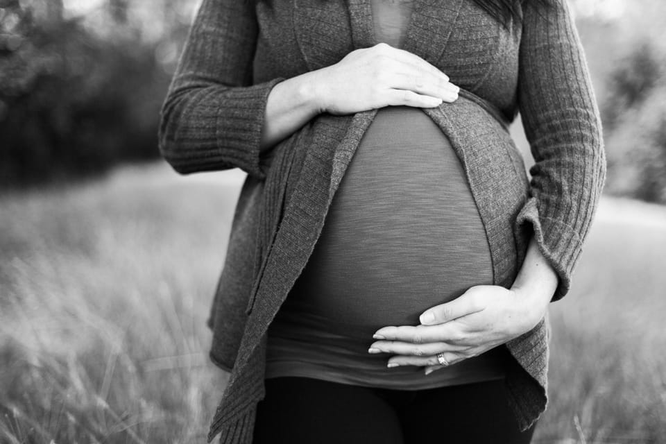 black and white photo of a pregnant woman standing in a grass field