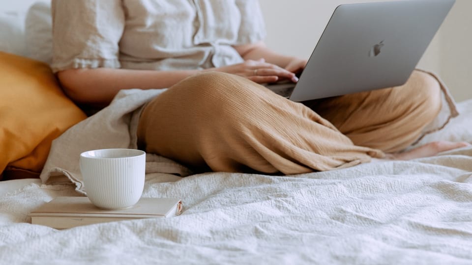 person-sitting-on-bed-using-laptop-with-mug